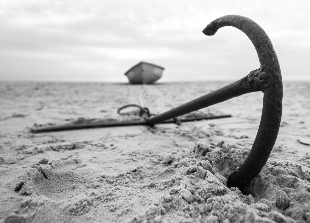 An anchor in the sand tethered to a boat in the distance.